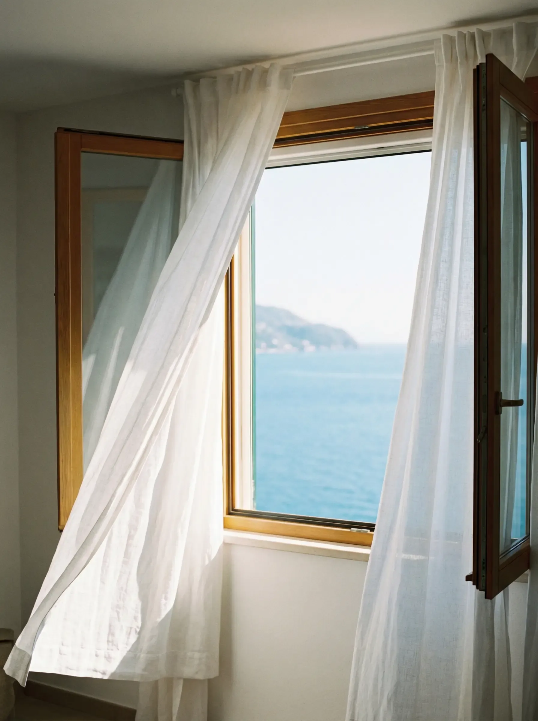 Ventana abierta con cortinas de lino blanco al viento mirando al mar mediterráneo